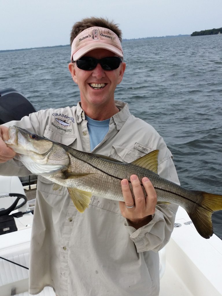 One of Captain Morgan Fishing Charters smiling during a fishing trip in Boca Grande holding a medium sized fish.